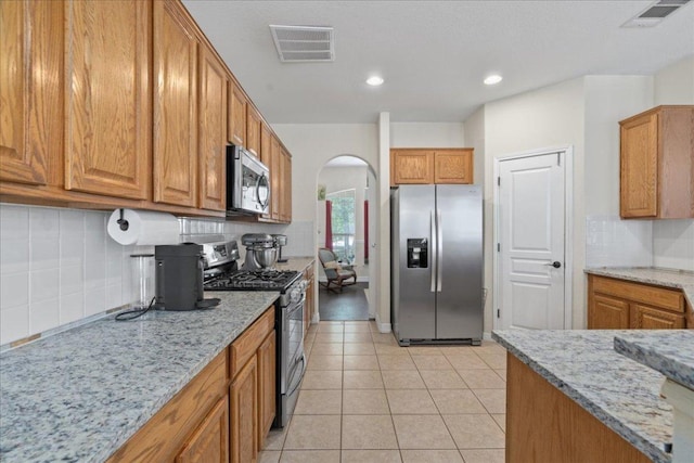kitchen with arched walkways, appliances with stainless steel finishes, brown cabinetry, and visible vents