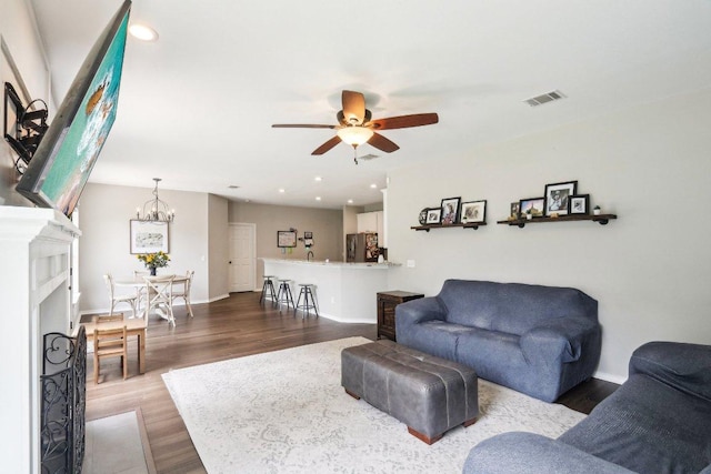 living area with baseboards, visible vents, ceiling fan with notable chandelier, and dark wood-type flooring