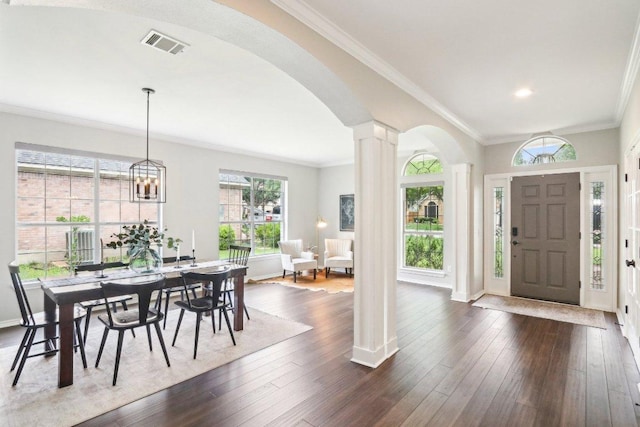 foyer entrance with visible vents, crown molding, dark wood-style flooring, ornate columns, and arched walkways
