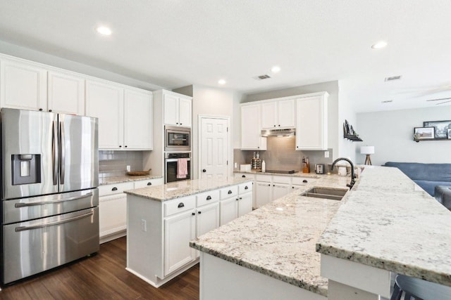 kitchen featuring decorative backsplash, a center island, under cabinet range hood, a sink, and appliances with stainless steel finishes