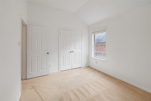 unfurnished bedroom featuring carpet floors, baseboards, lofted ceiling, and a closet