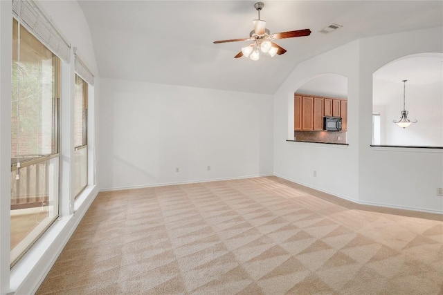 unfurnished living room featuring a ceiling fan, light colored carpet, visible vents, arched walkways, and lofted ceiling
