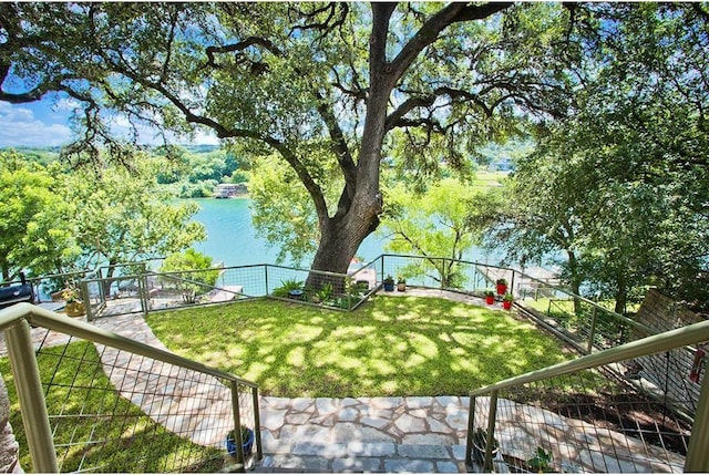 view of community featuring a water view, a fenced backyard, and a yard