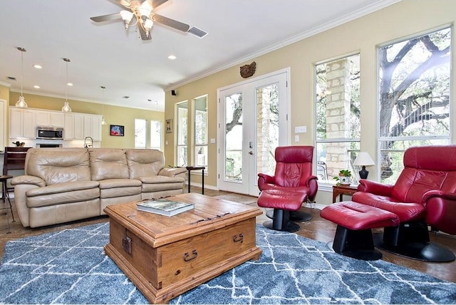 living area with ceiling fan, visible vents, ornamental molding, and a wealth of natural light