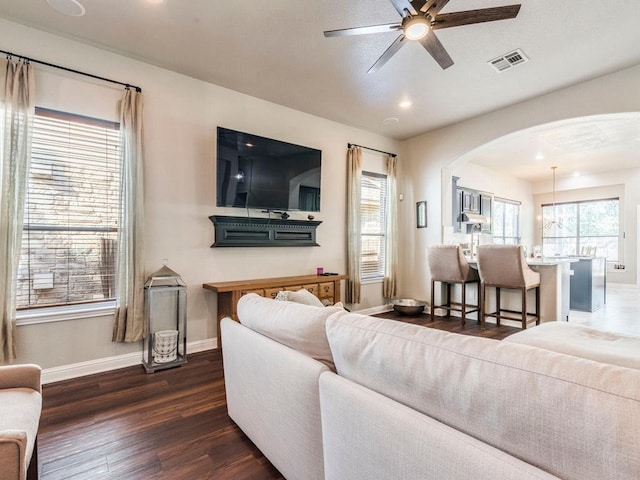 living room with a ceiling fan, visible vents, arched walkways, baseboards, and dark wood-type flooring