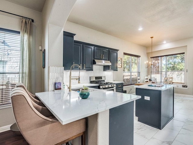 kitchen featuring a notable chandelier, a sink, stainless steel gas range oven, under cabinet range hood, and a kitchen island