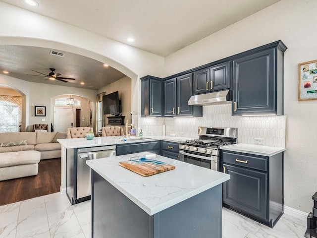 kitchen featuring marble finish floor, arched walkways, under cabinet range hood, a sink, and stainless steel appliances
