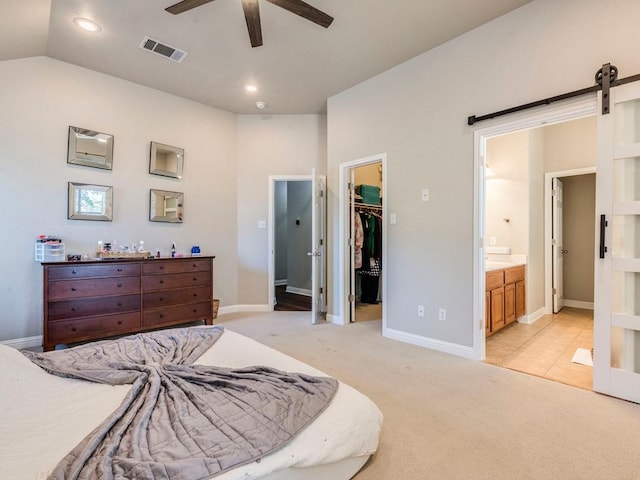 bedroom featuring a walk in closet, visible vents, a barn door, baseboards, and light carpet