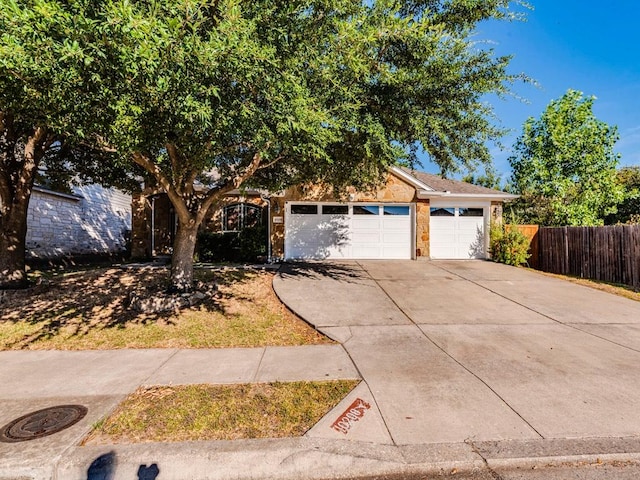 view of property hidden behind natural elements with fence, an attached garage, and driveway