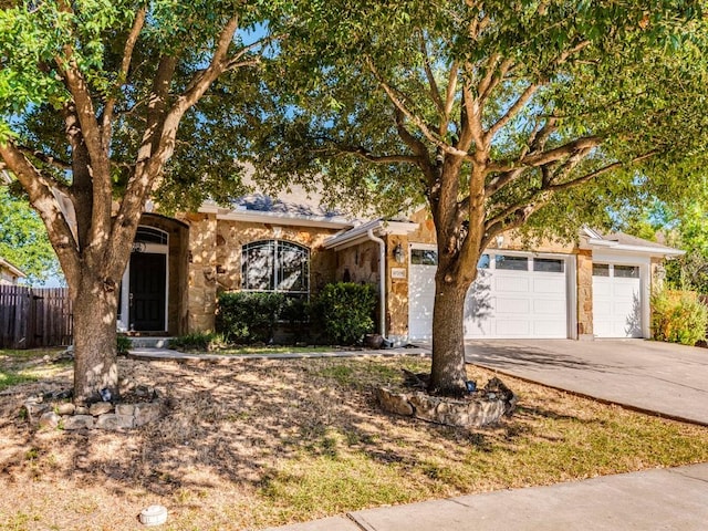 view of property hidden behind natural elements featuring fence, an attached garage, driveway, and stone siding