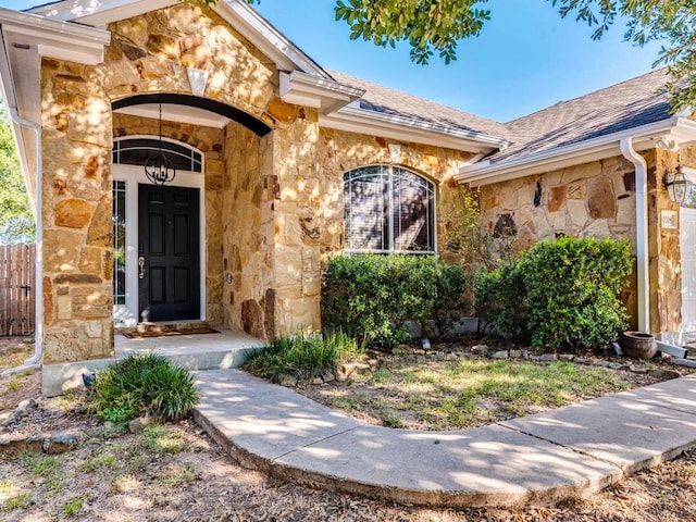 doorway to property featuring roof with shingles, fence, and stone siding