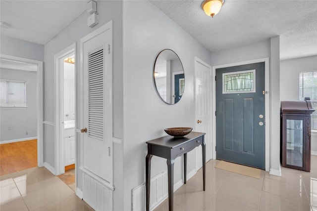 foyer entrance with a textured ceiling, baseboards, and light tile patterned floors