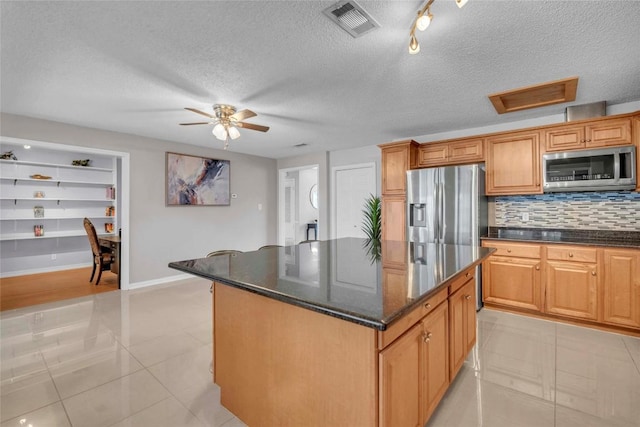 kitchen featuring decorative backsplash, appliances with stainless steel finishes, a center island, light tile patterned floors, and baseboards