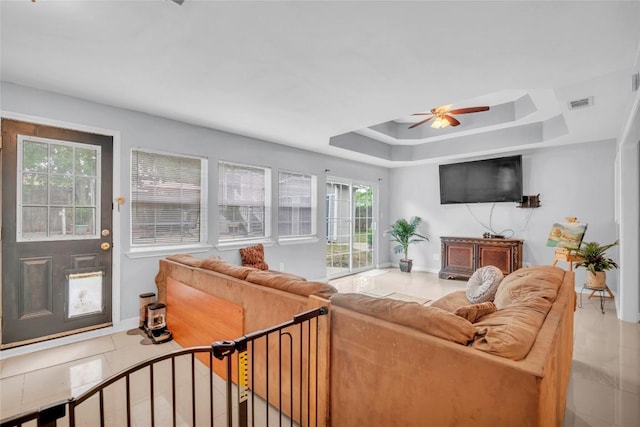 tiled living room featuring visible vents, a ceiling fan, baseboards, and a tray ceiling