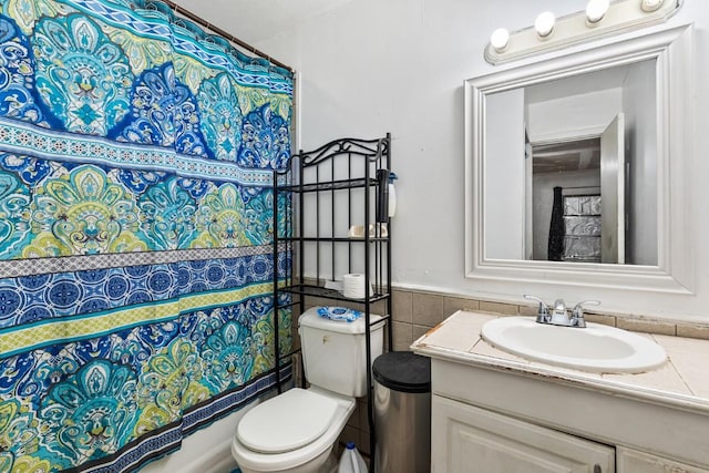 full bath with toilet, tile walls, wainscoting, and vanity