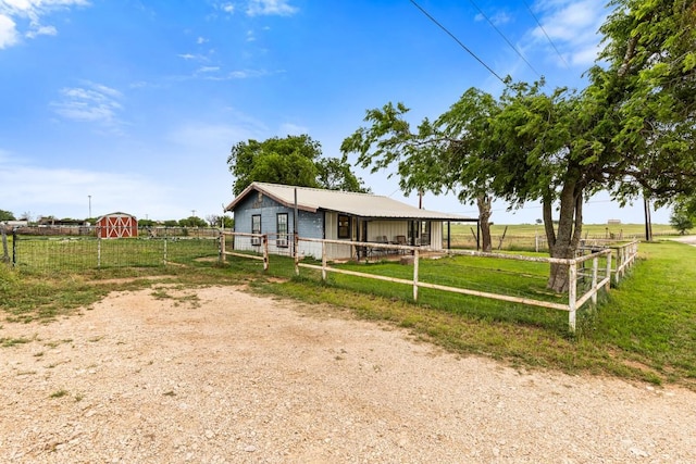 view of front of house featuring an outdoor structure, fence, driveway, and a rural view