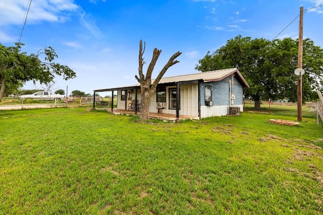 rear view of property featuring central AC, fence, a yard, and metal roof