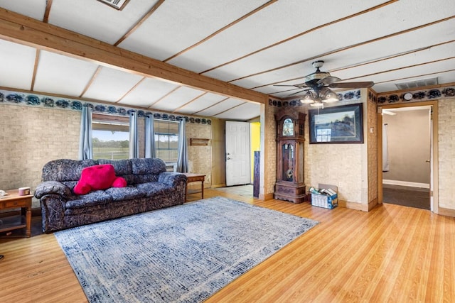 living room featuring wood finished floors, ceiling fan, brick wall, and visible vents