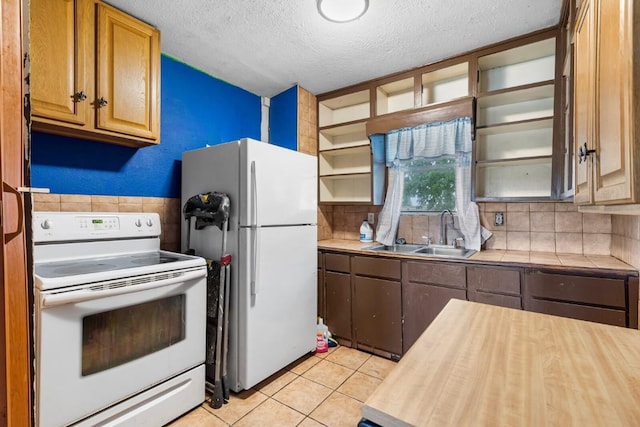 kitchen featuring a textured ceiling, a sink, light tile patterned floors, tile counters, and white appliances