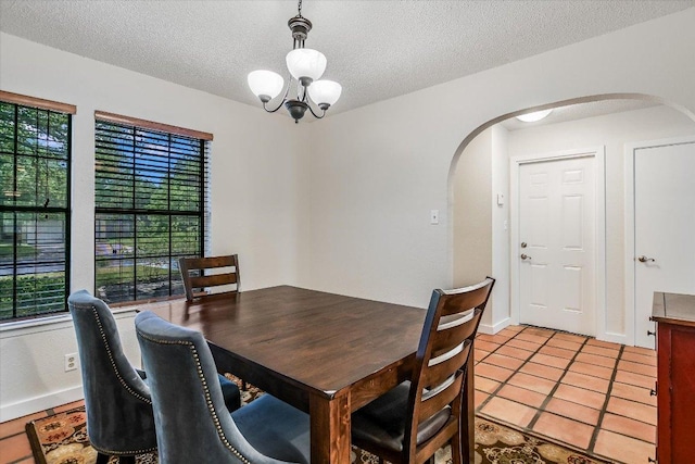 dining room featuring an inviting chandelier, arched walkways, a textured ceiling, baseboards, and light tile patterned floors