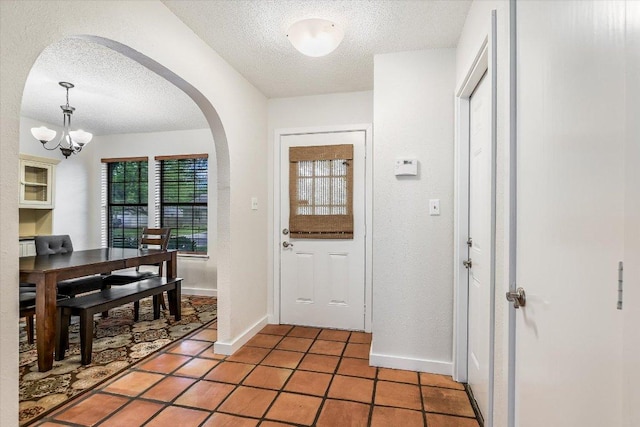 foyer featuring a textured ceiling, arched walkways, light tile patterned floors, baseboards, and a notable chandelier