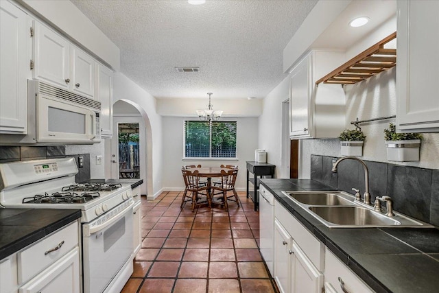 kitchen with a sink, arched walkways, tasteful backsplash, and white appliances