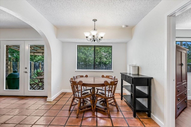 dining area featuring arched walkways, a textured ceiling, a chandelier, baseboards, and light tile patterned floors