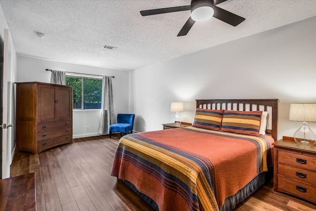 bedroom with a ceiling fan, a textured ceiling, visible vents, and hardwood / wood-style flooring