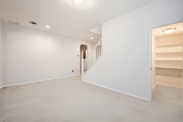 empty room featuring baseboards, arched walkways, and light carpet
