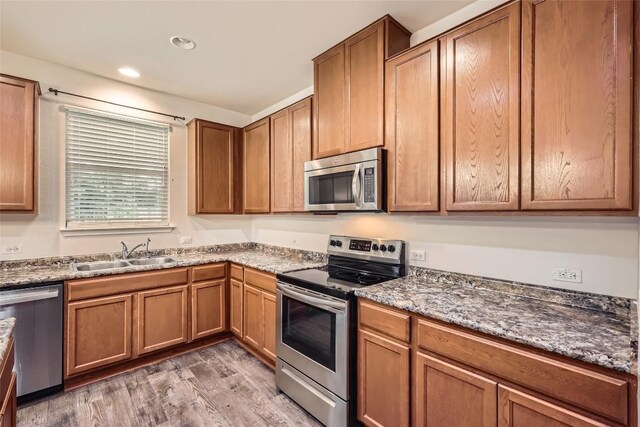 kitchen with light wood-type flooring, a sink, brown cabinetry, and appliances with stainless steel finishes