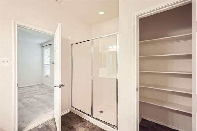 full bathroom with a walk in closet, baseboards, a shower stall, and wood finished floors