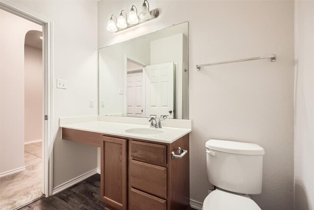 half bathroom featuring toilet, baseboards, wood finished floors, and vanity
