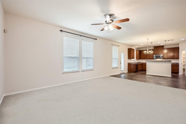 unfurnished living room with dark colored carpet, recessed lighting, baseboards, and ceiling fan with notable chandelier