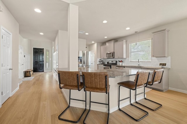 kitchen with appliances with stainless steel finishes, light wood-style floors, stone countertops, decorative backsplash, and a kitchen bar