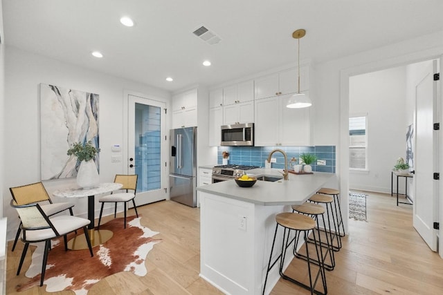 kitchen with a sink, stainless steel appliances, light wood-style flooring, and visible vents