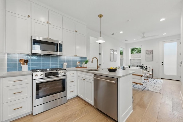 kitchen with appliances with stainless steel finishes, a sink, white cabinets, a peninsula, and light wood finished floors