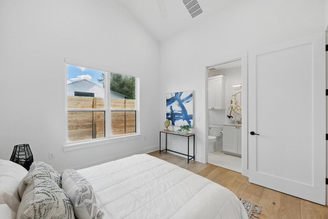 bedroom with visible vents, connected bathroom, light wood finished floors, and high vaulted ceiling