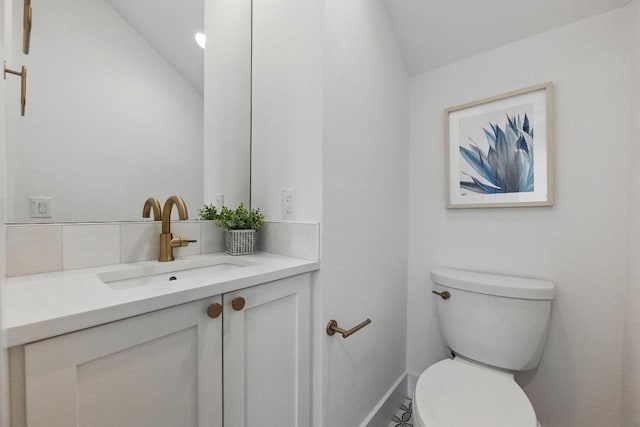 half bath with vanity, baseboards, vaulted ceiling, and toilet