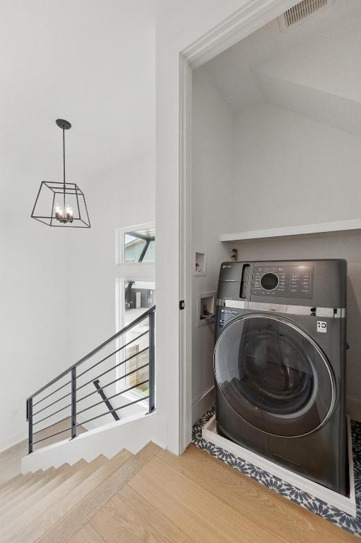 laundry area featuring an inviting chandelier, wood finished floors, washer / clothes dryer, and visible vents