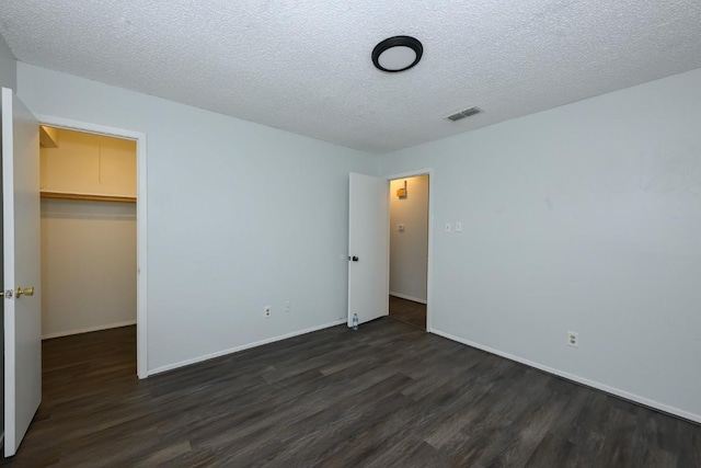 7103 Howerington Cir, Austin, TX 78724 - unfurnished bedroom featuring dark wood-style flooring, a walk in closet, a textured ceiling, a closet, and baseboards