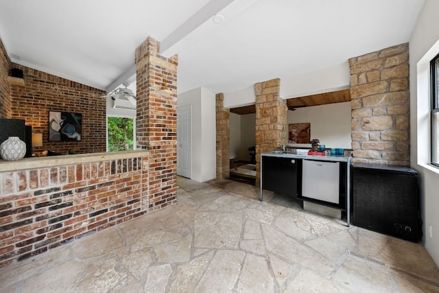 interior space with a sink, brick wall, stone finish floor, decorative columns, and lofted ceiling