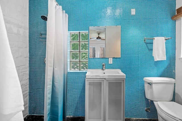 bathroom featuring ceiling fan, vanity, toilet, a heating unit, and tile walls