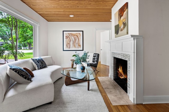 living room featuring a premium fireplace, baseboards, wooden ceiling, and wood finished floors
