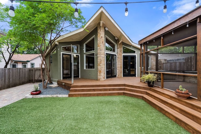 rear view of property with fence, a deck, a lawn, and french doors