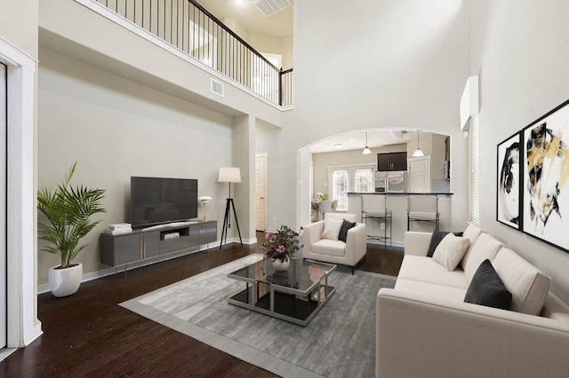 living area featuring arched walkways, a high ceiling, wood-type flooring, and visible vents