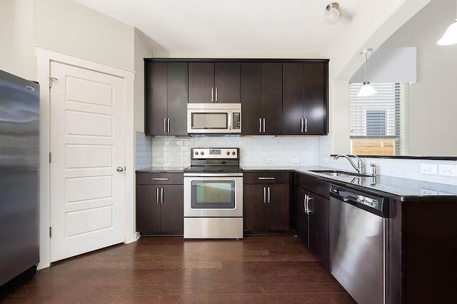 kitchen with dark brown cabinetry, appliances with stainless steel finishes, a sink, backsplash, and dark wood-style floors
