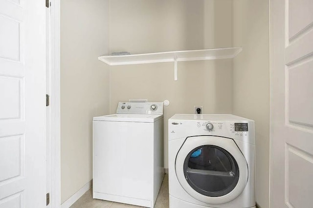 clothes washing area featuring light tile patterned floors, baseboards, and washer and dryer