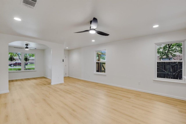unfurnished living room with a healthy amount of sunlight, arched walkways, a ceiling fan, and light wood finished floors
