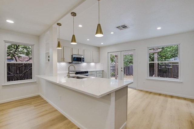 kitchen featuring stainless steel microwave, tasteful backsplash, french doors, a sink, and light wood-style flooring