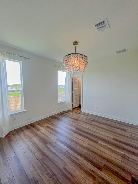 spare room featuring visible vents, baseboards, wood finished floors, and an inviting chandelier